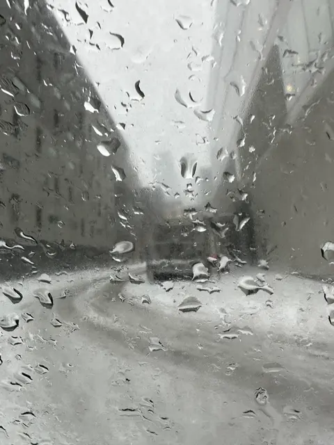 قطرات مطر على نافذة تلطّف أشكال الشارع وراءها.